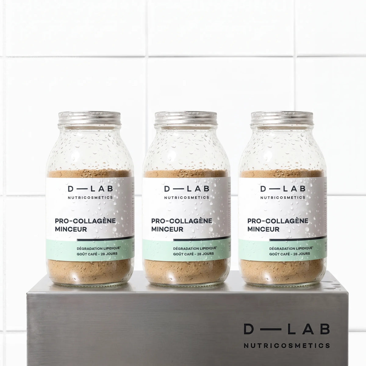 Cure 3 mois Pro-Collagène Minceur goût café D-LAB, trois flacons en verre alignés sur socle en métal brossé, fond carrelage blanc