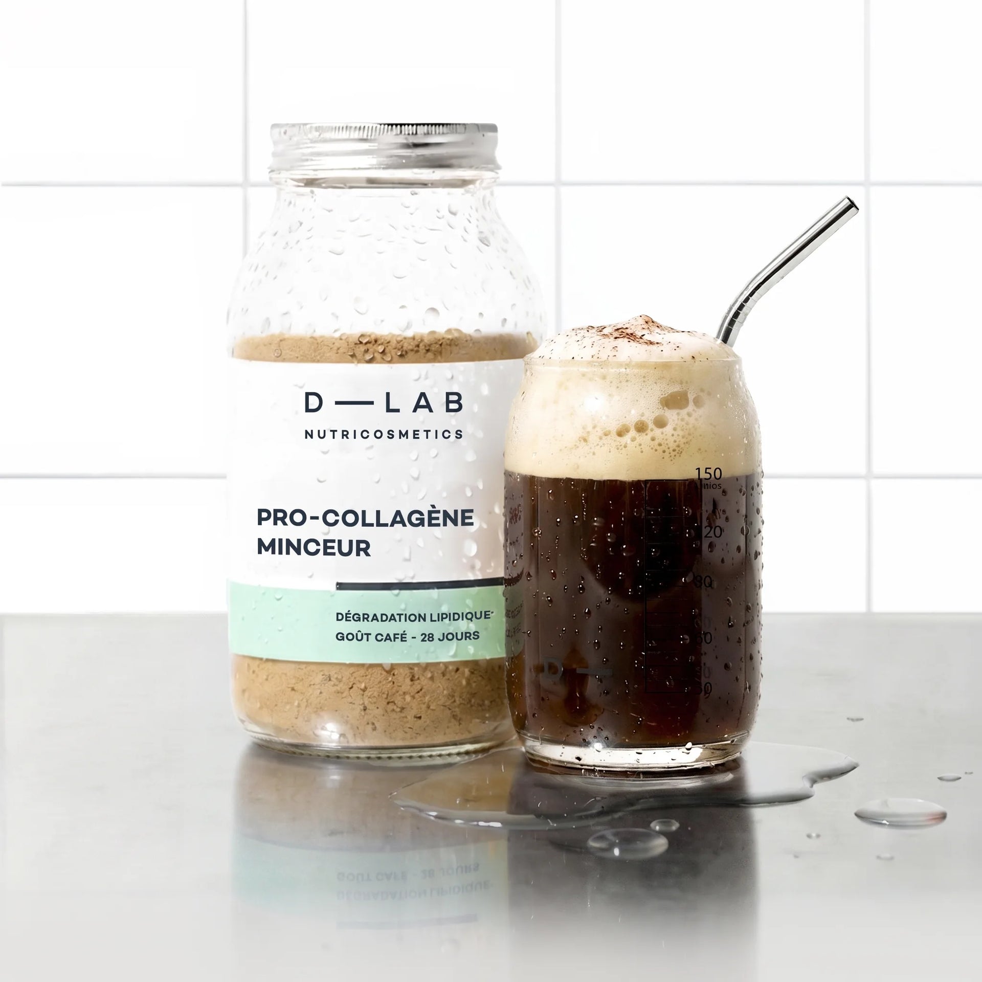 Flacon en verre Pro-Collagène Minceur goût café D-LAB et verre de boisson au café moussée avec paille inox, sur plan de travail carrelé blanc