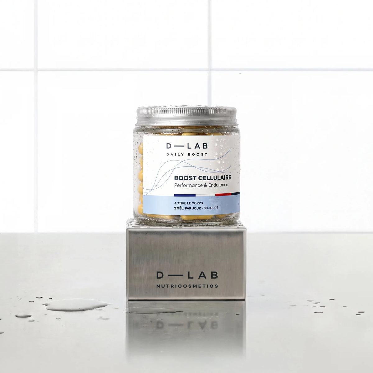Boost Cellulaire Daily Boost D-LAB Nutricosmetics, cure 1 mois : flacon de gélules posé sur un socle inox brossé, fond carrelage blanc
