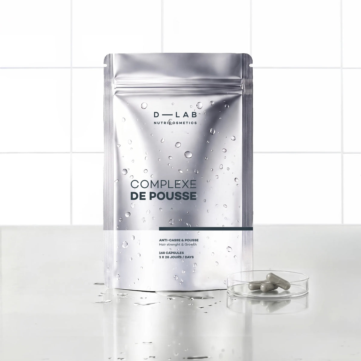 Complexe de Pousse D-LAB Nutricosmetics cure 3 mois, doypack argenté de 240 capsules accompagné d'une coupelle de gélules, fond carrelage blanc