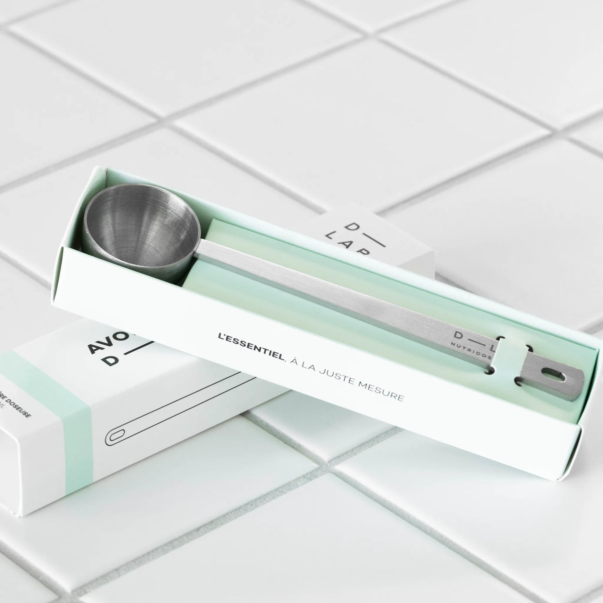 Étui ouvert de la cuillère doseuse D-LAB Nutricosmetics, cuillère en inox brossé gravée du logo, mention « L'essentiel à la juste mesure »