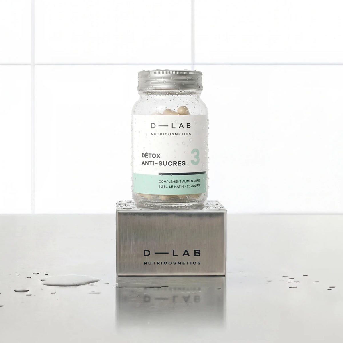 Détox Anti-Sucres D-LAB Nutricosmetics, cure 1 mois : flacon de gélules posé sur un socle inox brossé, fond carrelage blanc