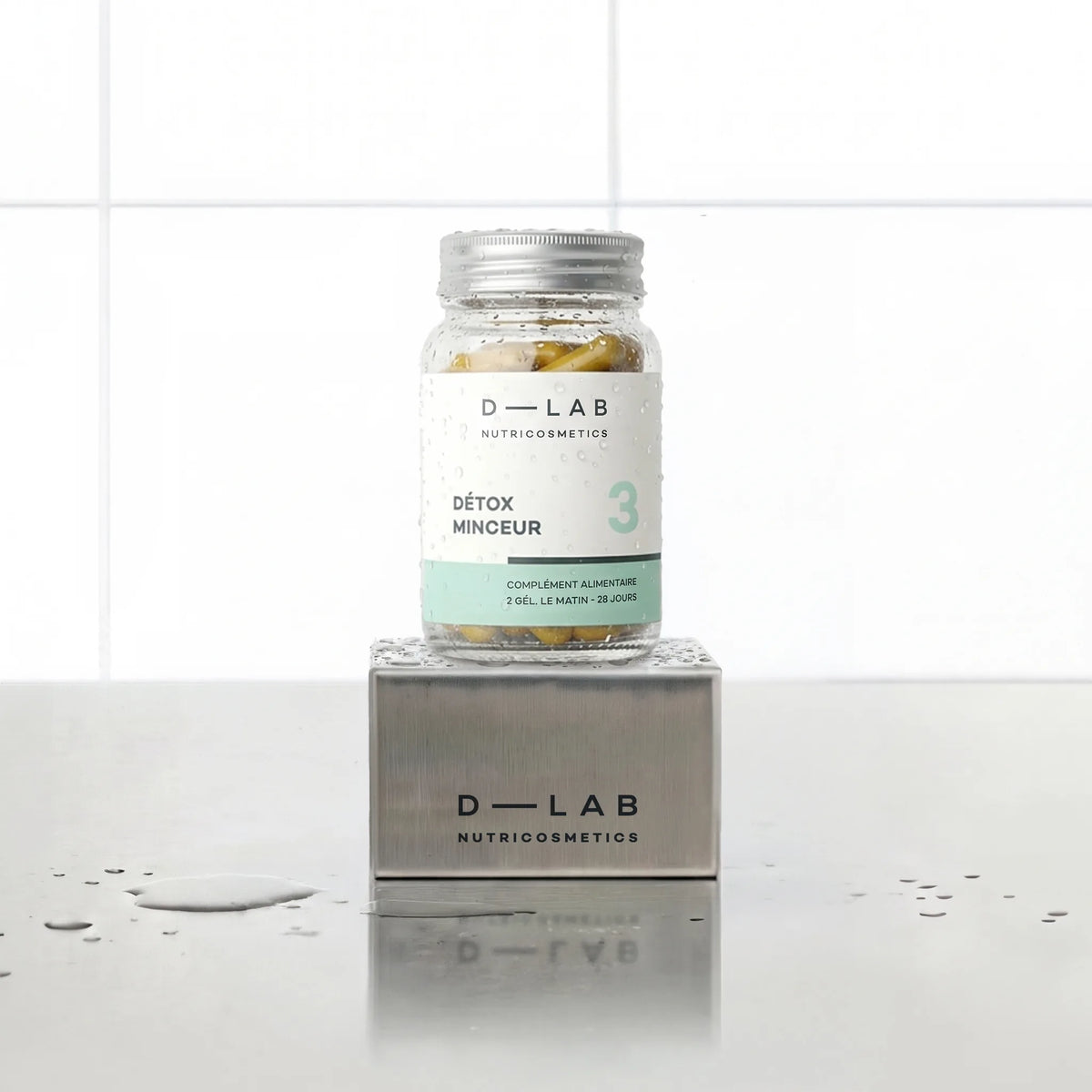Détox Minceur D-LAB Nutricosmetics, cure 1 mois : flacon en verre de gélules posé sur un socle inox brossé, fond carrelage blanc