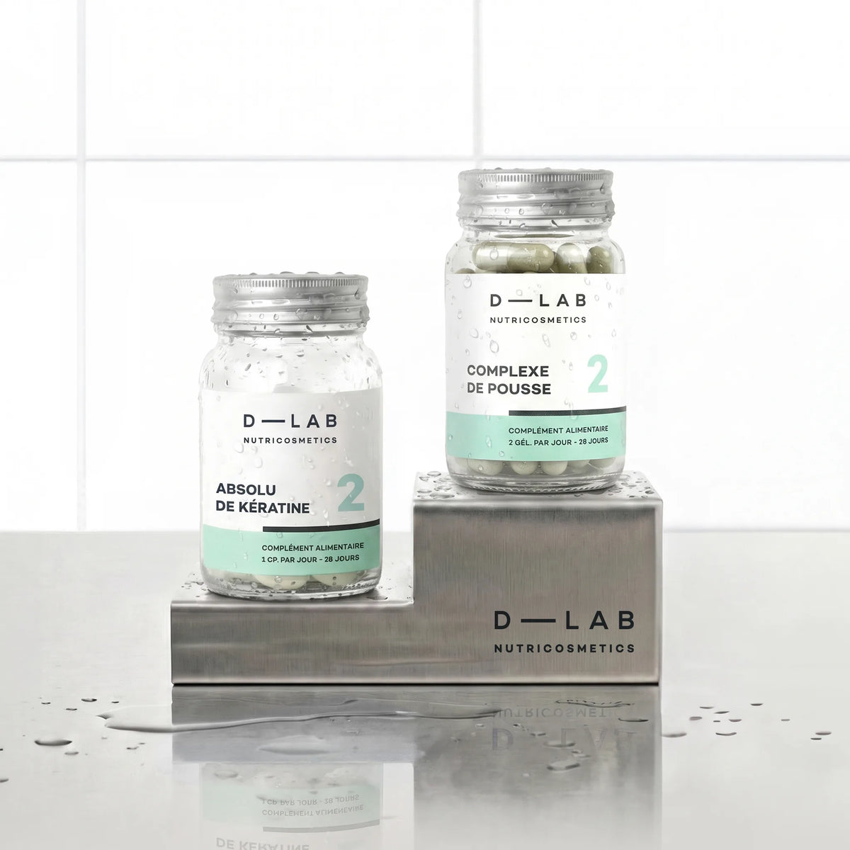 Routine Nutrition-Capillaire D-LAB cure 1 mois, duo Absolu de Kératine et Complexe de Pousse en flacons verre sur socles inox brossé, fond carrelage blanc