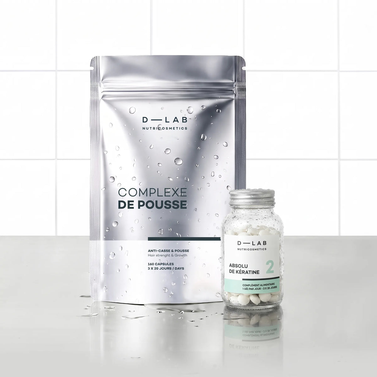 Routine Nutrition-Capillaire D-LAB cure 3 mois, doypack Complexe de Pousse et flacon Absolu de Kératine côte à côte, décor carrelage blanc et reflets d'eau