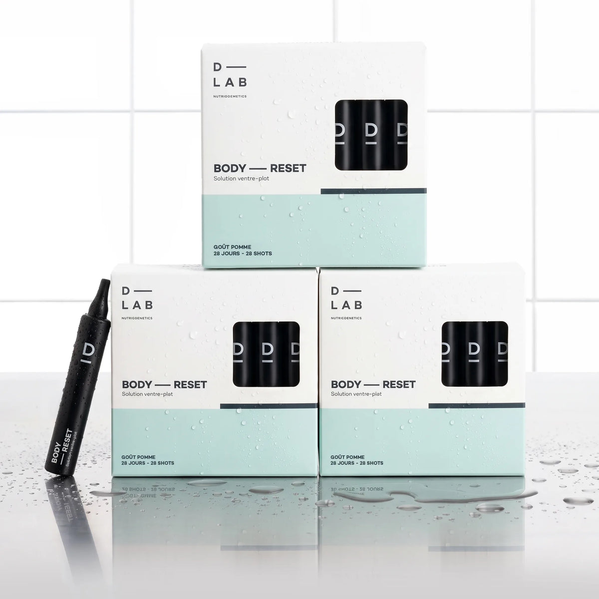 Solution Ventre-Plat Body-Reset D-LAB cure 3 mois, trois étuis de 28 shots empilés en pyramide avec un shot noir au premier plan, fond carrelage blanc