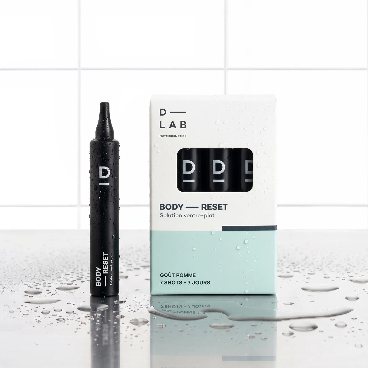 Solution Ventre-Plat Body-Reset D-LAB cure 7 jours, shot noir devant son étui blanc et vert d'eau 7 shots goût pomme, fond carrelage blanc